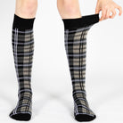 Person wearing black knee-high socks with tartan pattern on a white background