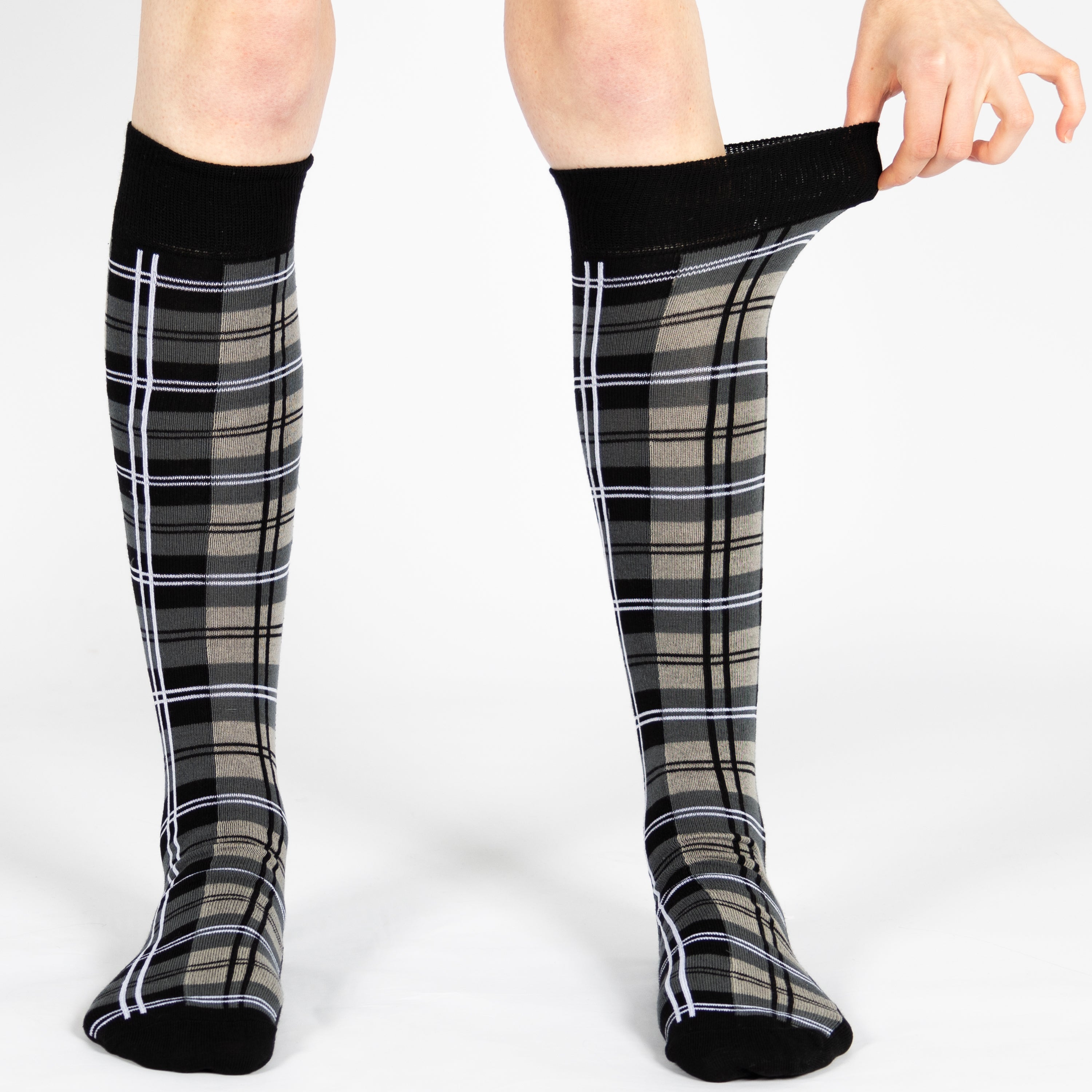 Person wearing black knee-high socks with tartan pattern on a white background